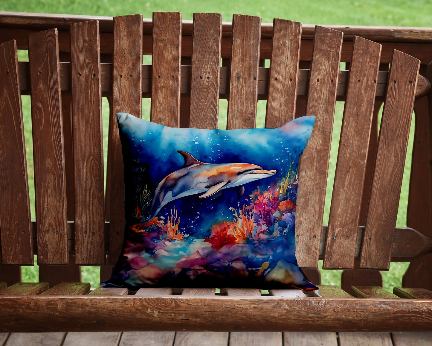 A dolphin watercolor pillow on a wooden bench with a grassy background.