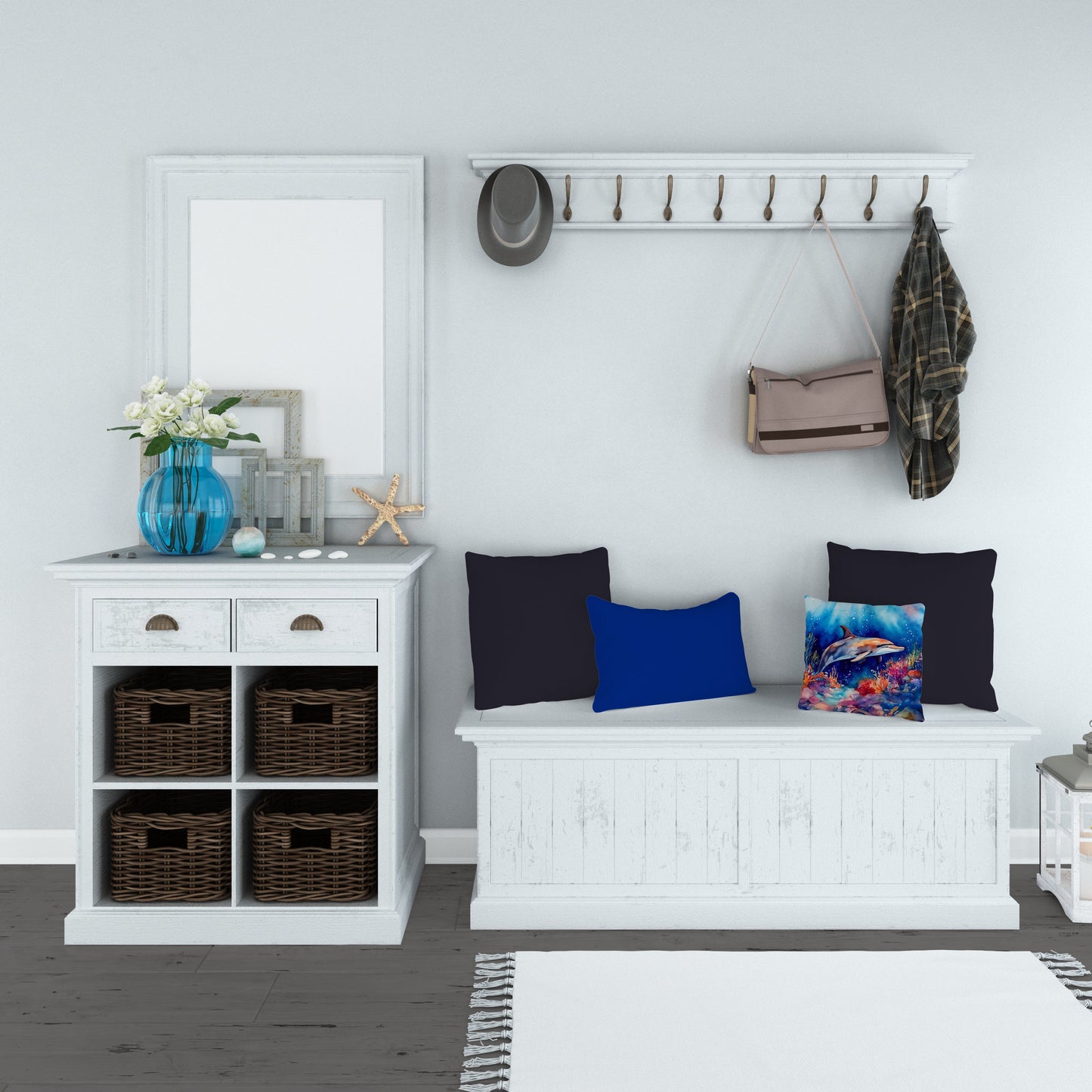 A hallway scene with a white console table topped with a blue vase, frames, and a starfish. Above, there's a coat rack holding a hat, a bag, and a plaid shirt. A white bench with blue and marine-themed pillows sits below, and a white rug lies on the dark wood floor.